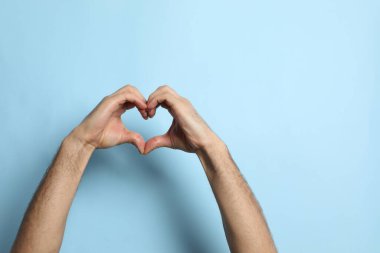Elleri açık mavi arkaplanda kalp yapan adam, yakın plan. Metin için boşluk