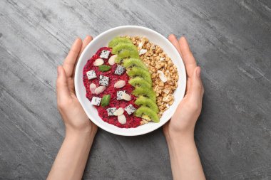 Elinde bir kase granola, pitahaya, kivi ve badem olan bir kadın var.