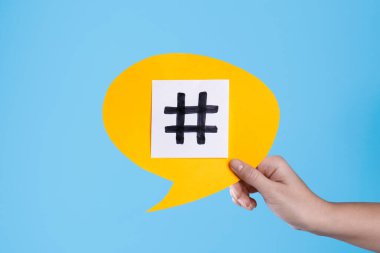 Turkuaz arka planda hashtag sembollü sarı kağıt konuşma balonu tutan kadın, yakın plan