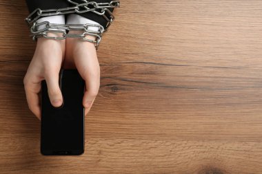 Ahşap masada zincire vurulmuş akıllı telefonu elinde tutan adam. İnternet bağımlılığı