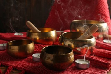 Tibetan singing bowls with mallets, candles and red fabric on wooden table clipart