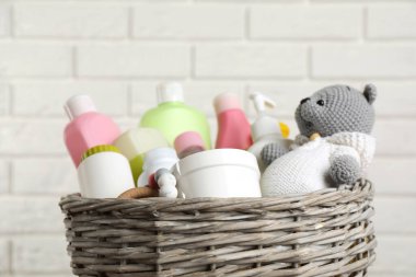 Beyaz tuğla duvara karşı farklı bebek kozmetik ürünleri ve oyuncaklarla dolu bir sepet.