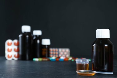 Bir şişe öksürük şurubu, kaşık uyuşturma ve siyah masada ölçme kabı. Metin için boşluk