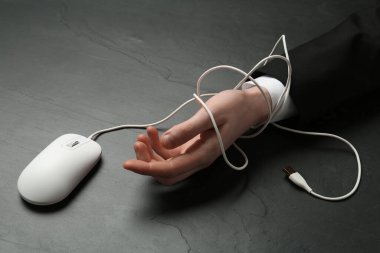 Siyah masadaki bilgisayar faresi kablosuyla bağlanmış bir adam, yakın plan. İnternet bağımlılığı