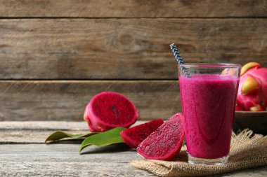 Bir bardak lezzetli pitahaya smoothie ve ahşap masada taze meyveler, metin için yer.