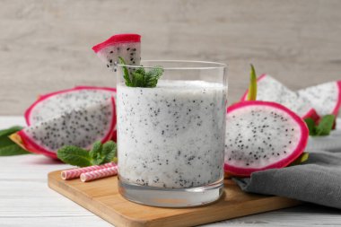 Bir bardak lezzetli pitahaya smoothie, ejderha meyveleri ve beyaz ahşap masada taze nane.