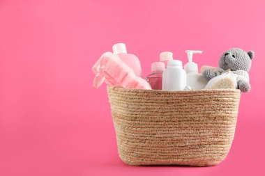Farklı bebek kozmetik ürünleri, banyo aksesuarları ve pembe arka planda hasır sepetin içinde oyuncak. Metin için boşluk