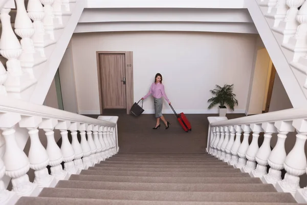 Otel koridorunda kırmızı valizli bir iş kadını.
