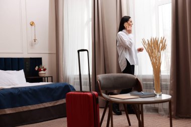 Güzel bir iş kadını otel odasının penceresinin yanında telefonla konuşuyor.