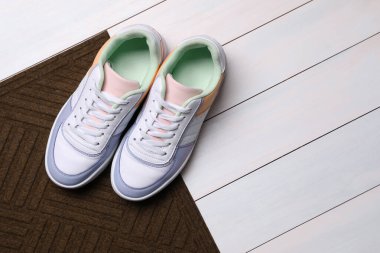 Yeni temiz kapı paspası, beyaz tahta zeminde ayakkabılar, düz yatış. Metin için boşluk