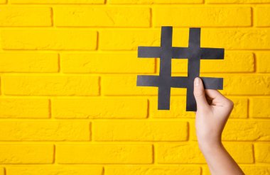 Sarı tuğla duvarda hashtag 'in siyah kağıt kesme sembolünü tutan kadın, yakın plan. Metin için boşluk