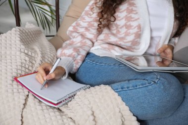 Not defteri ve tabletle evde yumurta sandalyesinde ders çalışan Afro-Amerikalı kadın, yakın plan. Uzaklık öğrenimi