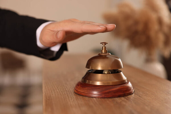 Man ringing service bell at wooden reception desk in hotel, closeup