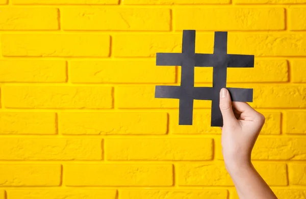 Mujer Sosteniendo Papel Negro Recorte Símbolo Hashtag Pared Ladrillo Amarillo — Foto de Stock