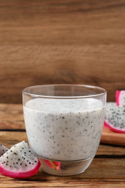 Bir bardak lezzetli pitahaya smoothie ve ahşap masada taze meyve.
