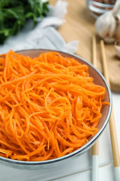 Delicious Korean carrot salad in bowl on white wooden table, closeup
