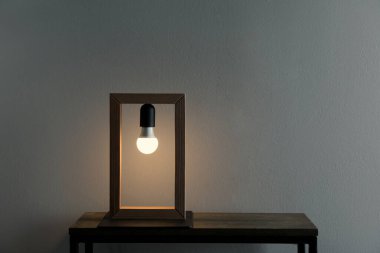Gri duvarın yanında modern lambalı ahşap masa, metin için yer var.