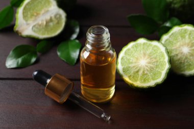 Bir şişe temel yağ, pipet ve ahşap masada taze bergamot meyveleri.