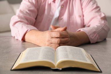 İncil 'i olan olgun bir kadın kapalı alandaki gri masada dua ediyor.