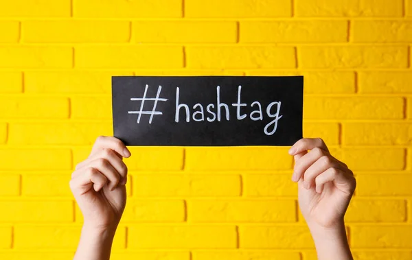 Mujer Sosteniendo Papel Negro Con Palabra Hashtag Símbolo Contra Pared — Foto de Stock
