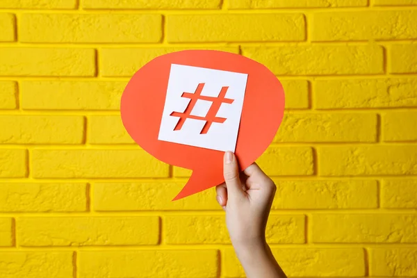Sarı Tuğla Duvara Hashtag Sembollü Kırmızı Kağıt Konuşma Balonu Tutan — Stok fotoğraf