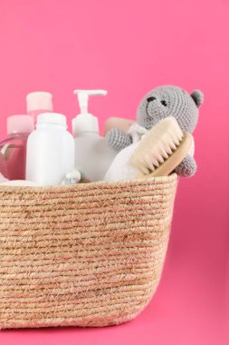 Farklı bebek kozmetik ürünleriyle dolu sepet, pembe arka planda saç fırçası ve oyuncak, yakın plan.