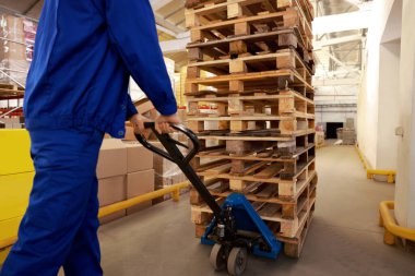 Depoda manuel forklift ile ahşap paletler taşıyan işçiler, yakın plan.