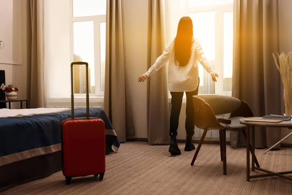 Young woman near window in hotel room, back view