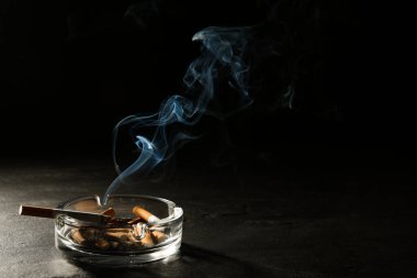 Siyah arka planda, gri masadaki cam kül tablasında sigara yakmak. Metin için boşluk