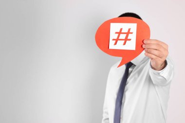 Açık arkaplanda yüzünün önünde hashtag sembolü olan kağıt konuşma balonu tutan adam. Metin için boşluk