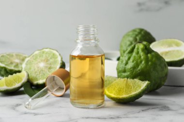 Beyaz mermer masada bir şişe temel yağ, pipet ve taze bergamot meyvesi.