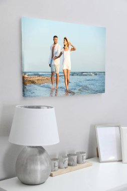 Odadaki beyaz duvarda genç bir çiftin basılı fotoğrafı olan tuval.
