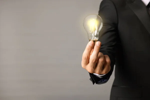 あなたの考えを上げなさい 灰色の背景に電球を保持するビジネスマンのクローズアップビュー テキストのためのスペース — ストック写真