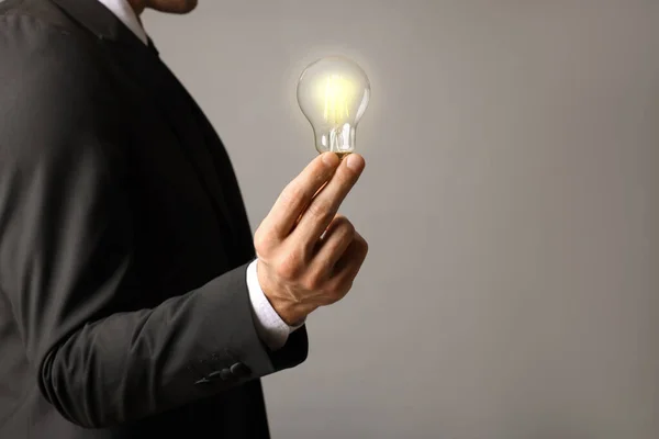 stock image Glow up your ideas. Closeup view of businessman holding light bulb on grey background, space for text