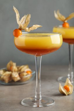 Gri masada bitki özü meyveleriyle süslenmiş lezzetli bir kokteyl.