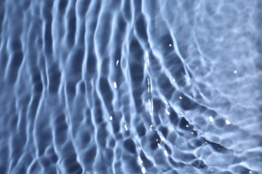 Mavi arkaplanda dalgalı yüzeyi olan suyun yakın görüntüsü