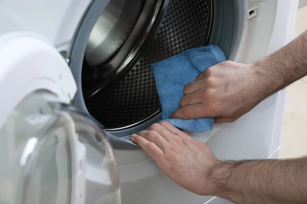 Man cleaning empty washing machine with rag, closeup