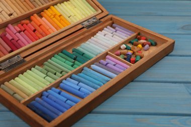Açık mavi ahşap masa üzerindeki kutuya pastel çizim, yakın plan.