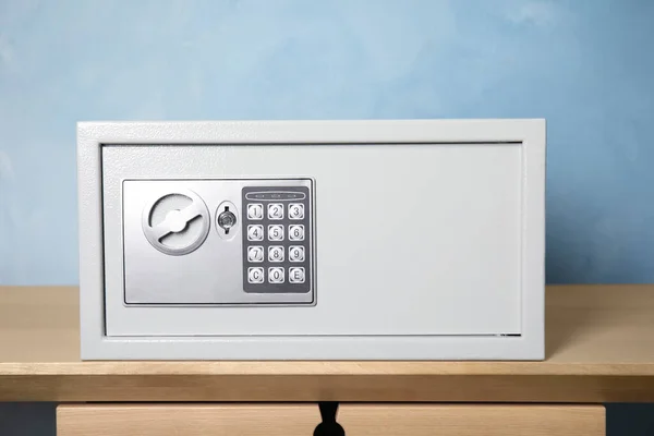 Closed steel safe on wooden table against light blue background