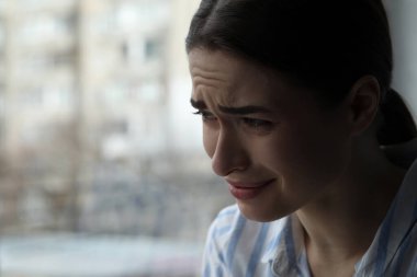 İçerideki pencerenin yanında ağlayan üzgün genç kadın, mesaj için yeri olan yakın plan. Yalnızlık kavramı