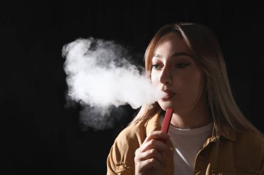 Siyah arka planda elektronik sigara kullanan genç bir kadın.