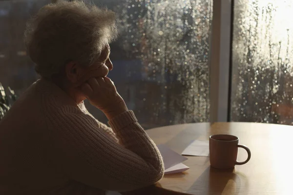 Mujer Mayor Con Bebida Mirando Por Ventana Interior Día Lluvioso — Foto de Stock