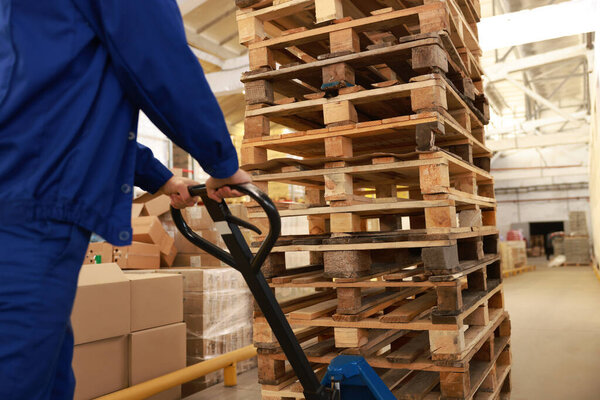 Worker moving wooden pallets with manual forklift in warehouse, closeup