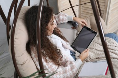 Tabletli Afro-Amerikalı kadın evde yumurta sandalyesinde ders çalışıyor. Uzaklık öğrenimi