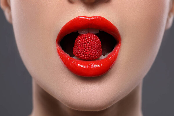 Young woman with red lips makeup eating candy on grey background, closeup