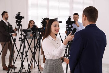 Profesyonel genç gazeteci arka planda iş adamı ve kamera operatörü grubuyla röportaj yapıyor.