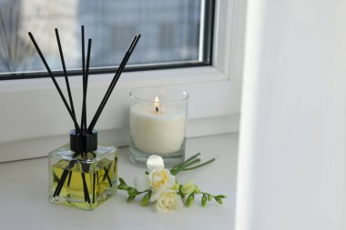 Aromatik kamış oda spreyi, frezya çiçekleri ve pencere kenarında yanan mum.