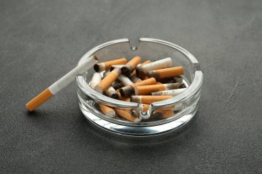 Gri masada sigara izmaritleriyle dolu cam kül tablası.