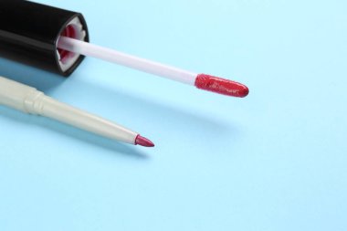 Açık mavi arka planda dudak kalemi ve sıvı ruj fırçası, yakın plan. Kozmetik ürünü