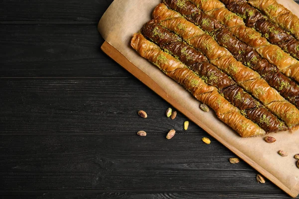 Delicious sweet baklava with pistachios on black wooden table, flat lay. Space for text